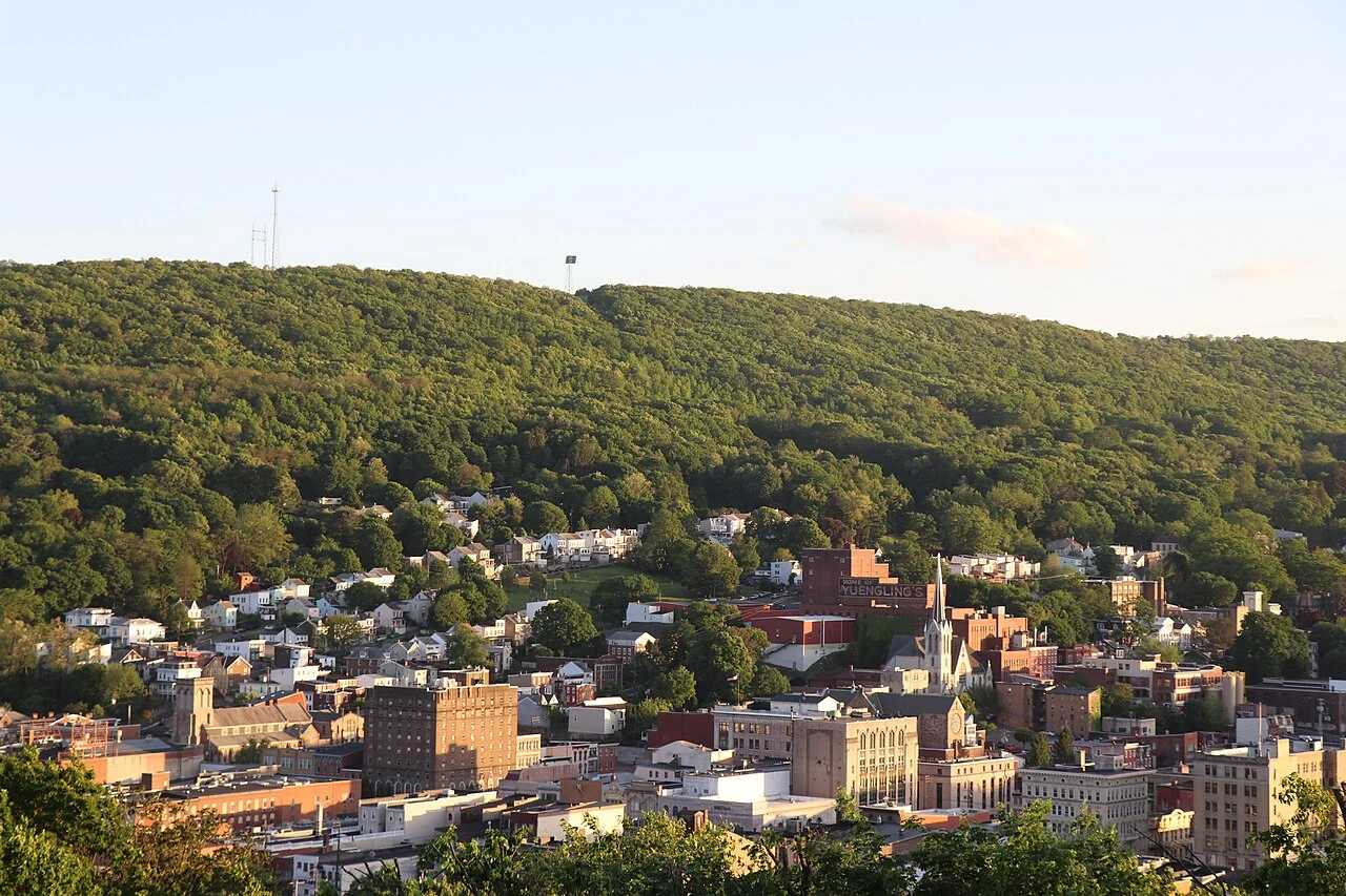 Pottsville's downtown buildings and church towers below wooded hills in Schuylkill County.